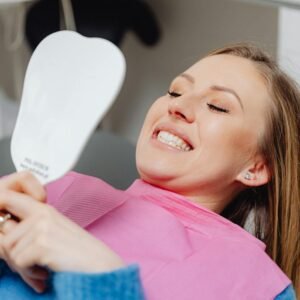 A woman at a dental clinic smiles while holding a mirror, showcasing her dental treatment results.